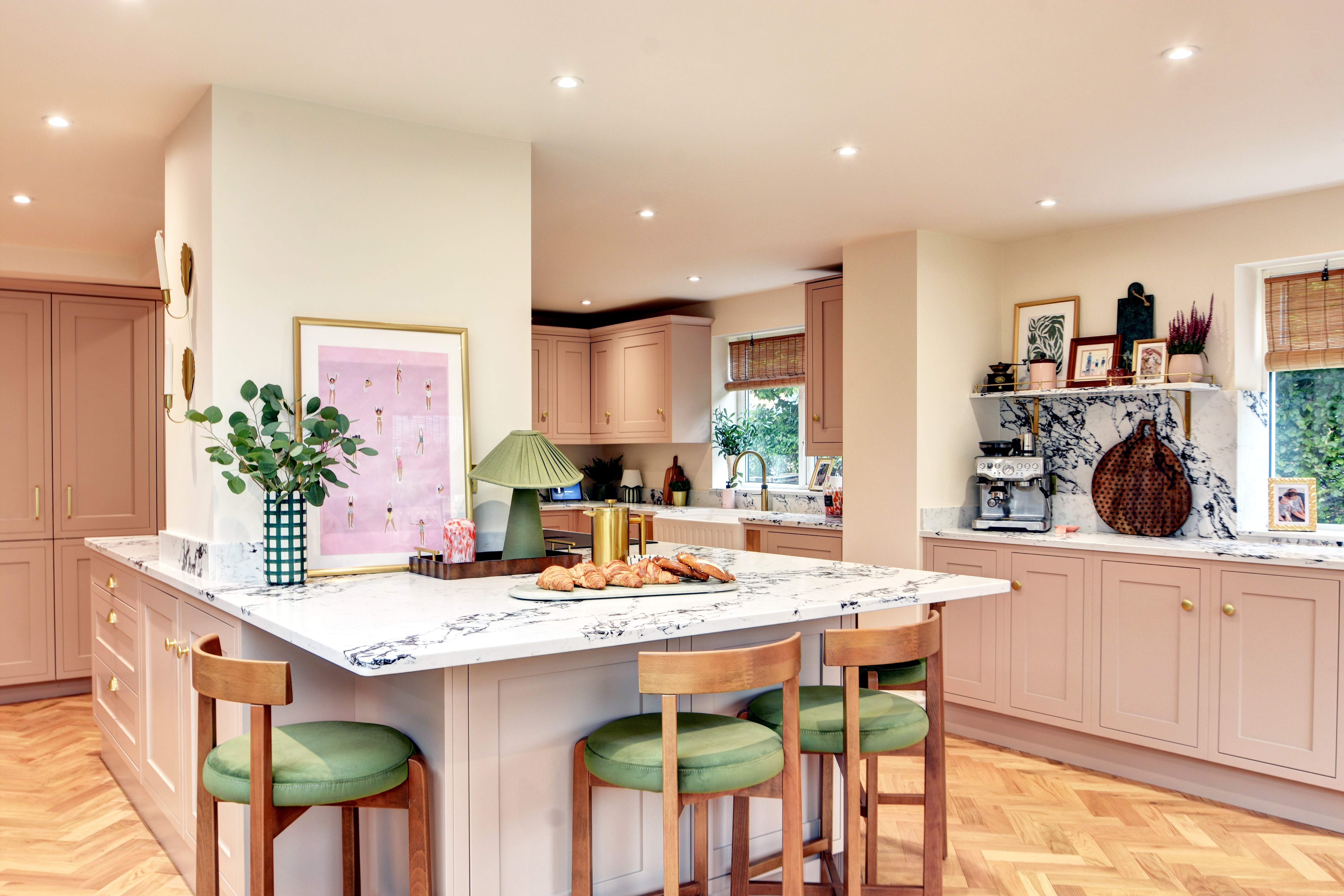Blush painted kitchen with marble worktops and green bar stools
