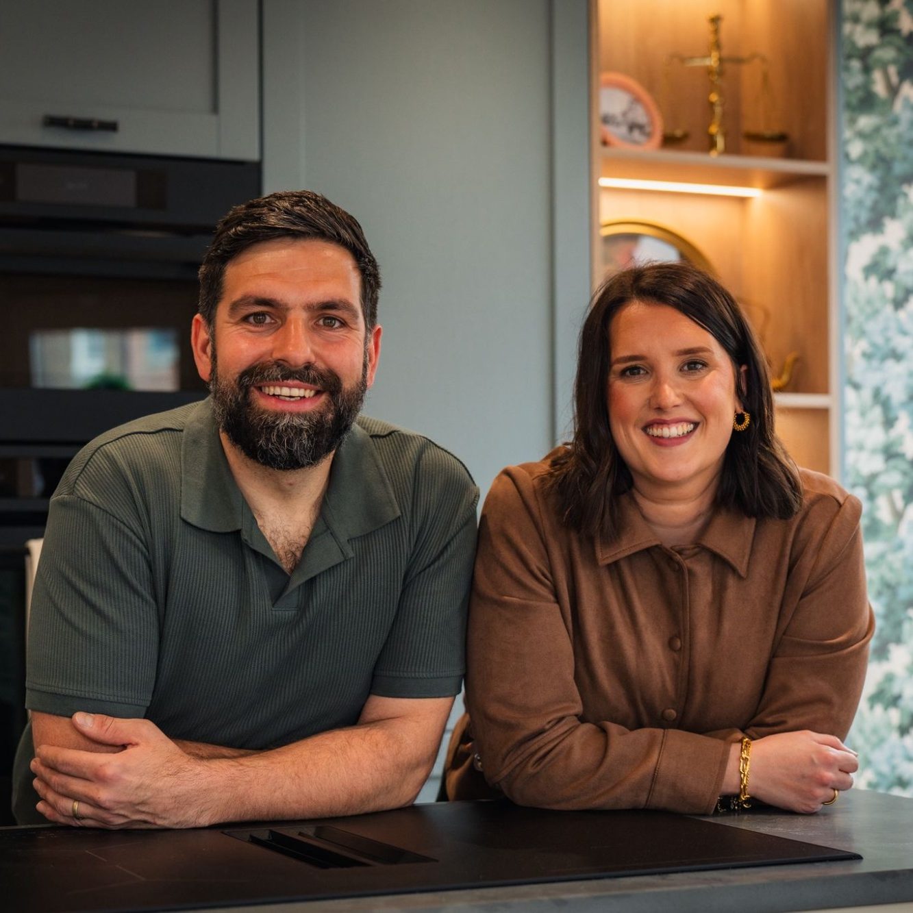 Sam and Hristiyan from The Kitchen Room seated at a kitchen island with fresh flowers, welcoming visitors to their Boroughbridge showroom